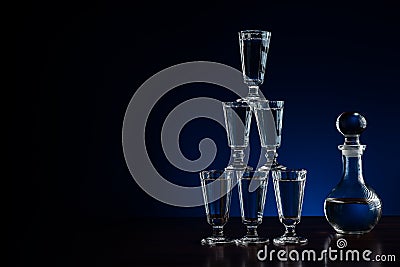 Crystal decanter or carafe of vodka and glasses pyramid tower on wooden table in restaurant, blue and black background with copy Stock Photo