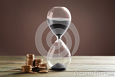 Crystal hourglass with black sand and coins on color wooden table. Time is money Stock Photo