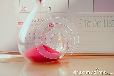 Crystal hourglass with red sand on calendar concept for time slipping away for important appointment date. Stock Photo