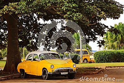 Cuba, Havana - January 16, 2019: Old yellow taxi car in the old city of Havana against the tropical tree Editorial Stock Photo