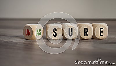 Cubes, dice or blocks with unsure and assure on wooden background Stock Photo