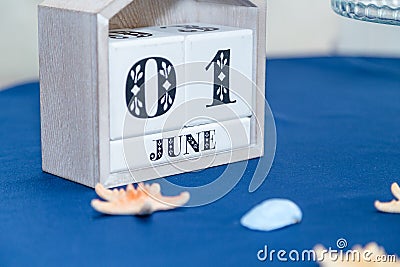 Cubic white wooden calendar with date 1 June standing on blue table cloth with some sea shells. Sea thematic party. Stock Photo