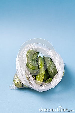 Cucumbers in plastic bag on blue background. Stop using artificial food storage bags concept Stock Photo