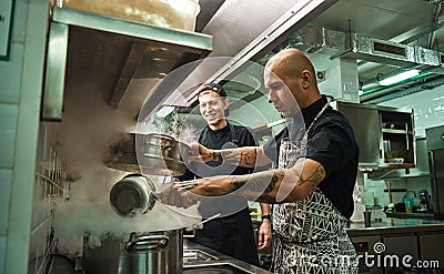 Culinary school. Handsome and confident chef teaching how to cook his two assistants in a restaurant kitchen Stock Photo