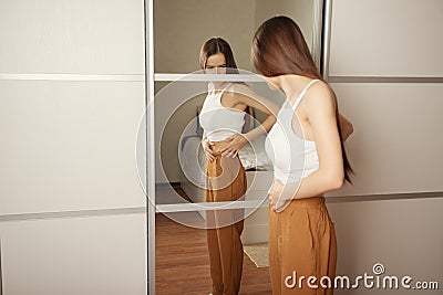 The cult of a beautiful body, public opinion, imposed stereotypes, A teenage girl is looking for fat on her body, stands at home Stock Photo