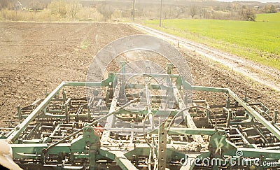 Cultivator behind tractor on ploughed soil near green field Stock Photo