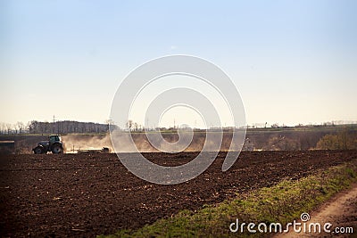 cultivator raises dust on ploughed field near ground road Stock Photo