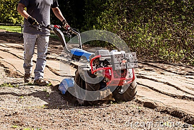 Rototiller tractor unit preparing soil dirt on outdoor garden Stock Photo