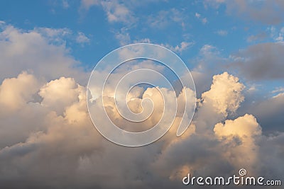 Cumulonimbus clouds against the blue sky. Picturesque cumulus clouds in the yellow light of the setting sun. Dramatic Stock Photo