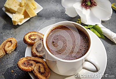 Cup of black coffee on a saucer with cookies, pieces of cheese, Magnolia flower on a gray background Stock Photo