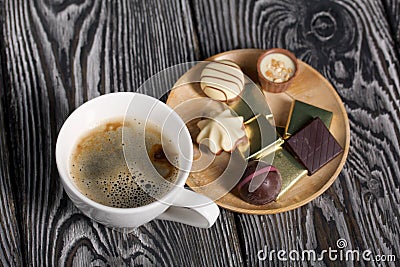 A cup of black coffee in a white cup. Chocolate in foil and chocolates. On pine boards Stock Photo