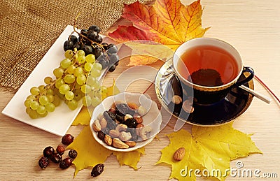 Cup of black tea, nuts, black and white grapes, red and yellow leaves, dried canker berry Stock Photo