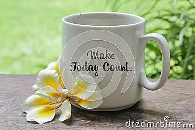 A cup of coffee with Bali frangipani flower on the wooden table with inspirational motivational quote on it - Make today count. Stock Photo