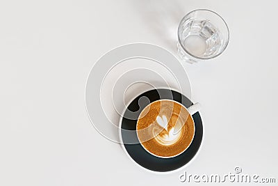 Cup of coffee on black saucer and glass of water on white background. Fresh cappuccino with beautiful latte art in shape Stock Photo