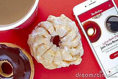 A cup of coffee with a Chocolate Dip Donut and Honey Cruller Donut with an iPhone Plus and the Tim Hortons app Editorial Stock Photo