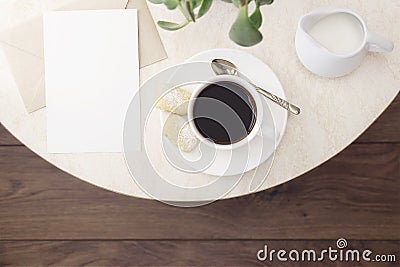 A cup of coffee with cookies, a silver spoon, milk, an empty letterhead with an envelope on a marble table in a cafe. Stock Photo