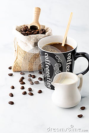 A cup of coffee with cream in front and a burlap sack of coffee beans in behind. Coffee break concept. Stock Photo