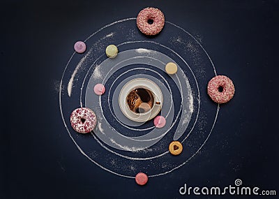 A cup of coffee, donuts and multi-colored macaroons in the form of a planetary system on a dark blue background Stock Photo