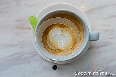 A cup of latte coffee with heart pattern in a white cup on white marble background and green sugar stick Stock Photo