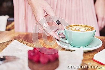 Cup of coffee latte and sweet pastry on wooden table in woman hands. Gentle romantic mood, girl wearing pink skirt. Stock Photo