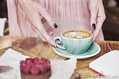 Cup of coffee latte and sweet pastry on wooden table in woman hands. Gentle romantic mood, girl wearing pink skirt. Stock Photo