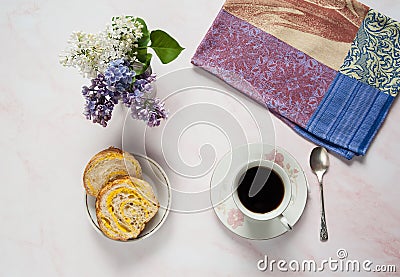 A cup of coffee, lilac flowers Syringa vulgaris and a sweet homemade turmeric bun on a pastel pink marble background. Stock Photo