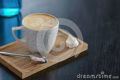 Cup of coffee on the little board over black background. Latte art. Little coffee mug and spoon. Stock Photo