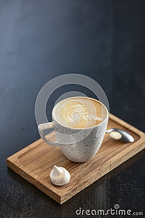 Cup of coffee on the little board over black background. Latte art. Little coffee mug and spoon. Stock Photo