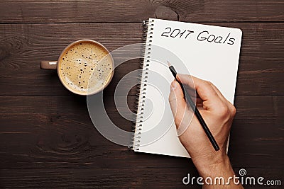 Cup of coffee and male hand writing in notebook goals for 2017. Planning and motivation for the new year concept. Top view. Stock Photo