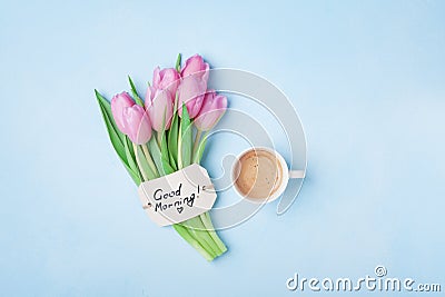 Cup of coffee, pink tulip flowers and note good morning on blue table top view. Beautiful breakfast on Mothers or Womans day. Stock Photo