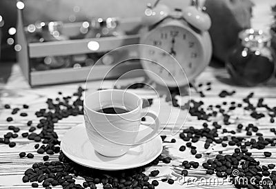 A cup of coffee on a platter with lots of sprinkled coffee beans. Alarm clock arrows at 9 am. Wooden textured table Stock Photo