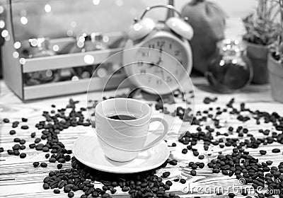 A cup of coffee on a platter with lots of sprinkled coffee beans. Alarm clock arrows at 9 am. Wooden textured table Stock Photo