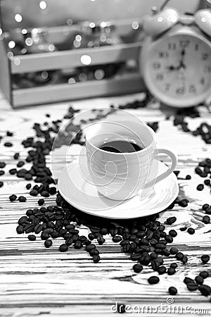 A cup of coffee on a platter with lots of sprinkled coffee beans. Alarm clock arrows at 9 am. Wooden textured table Stock Photo