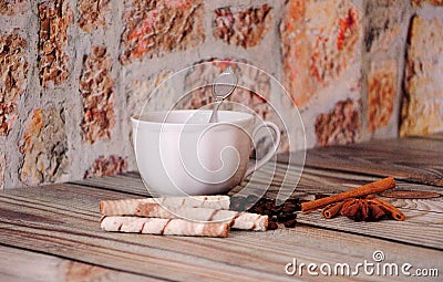 A cup of coffee, waffle rolls, anise, cinnamon and roasted coffee beans lie on a wooden table Stock Photo