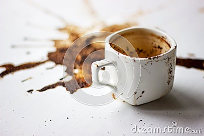 A Cup of custard coffee spilled on a white table background, side view. A beautiful spot from the coffee brew. Fortune Stock Photo