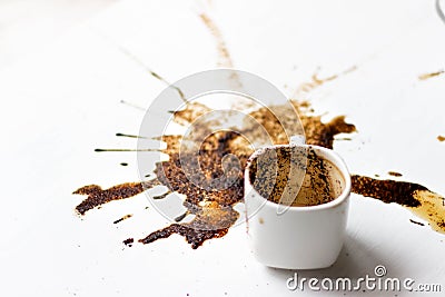 A Cup of custard coffee spilled on a white table background, side view. A beautiful spot from the coffee brew. Fortune Stock Photo