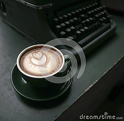 Cup of Flat White coffee in a green cup next to an old typewriter on green wood table Stock Photo