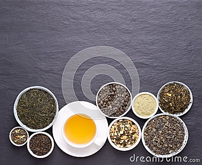 Cup of green tea and bowls of various dried tea leaves on dark, stone background Stock Photo