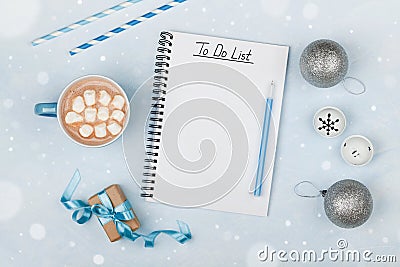 Cup of hot cocoa, gift, holiday decorations and notebook with to do list on blue vintage table from above, christmas planning. Stock Photo