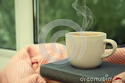 Cup of hot coffee, books and warm sweater on window sill indoors. Space for text Stock Photo