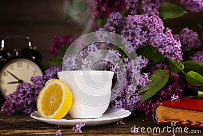 A cup of hot tea with a lemon and over a lilac flowers backdrop Stock Photo