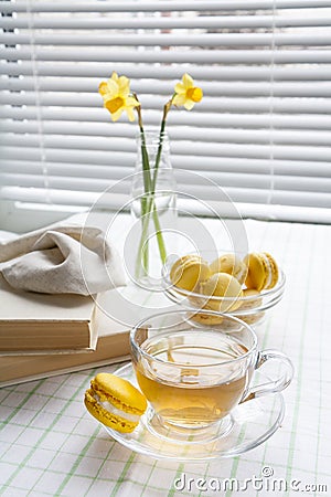 A cup of hot tea, yellow tulips, yellow daffodils, old books and lemon macaroons on a light background Stock Photo