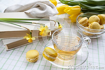 A cup of hot tea, yellow tulips, yellow daffodils, old books and lemon macaroons on a light background Stock Photo