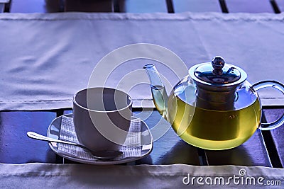 A cup of morning green tea. A transparent teapot with freshly brewed green tea and a white porcelain cup on the table by the windo Stock Photo