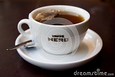 Cup of tea with Caffe Nero logo on white teacup with saucer and spoon on dark background. Editorial Stock Photo