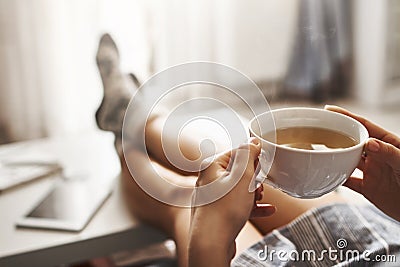 Cup of tea and chill. Woman lying on couch, holding legs on coffee table, drinking hot coffee and enjoying morning Stock Photo