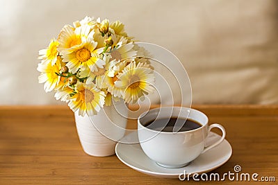 A cup of tea/coffee and a bouquet of daisies in a vase on a wooden tray on a light soft background Stock Photo