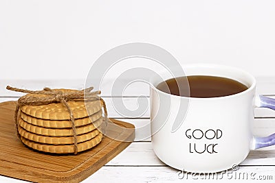 A cup of tea with the inscription good luck and a stack of crispy cookies on a wooden cutting board. Close-up Stock Photo