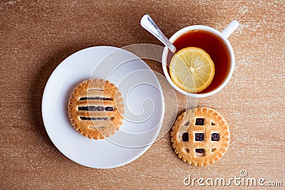 Cup of tea and lemon, cookies with jam in saucer on table top view Stock Photo