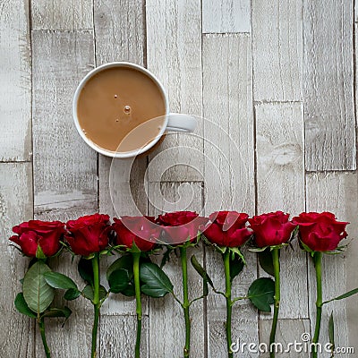 Cup of tea with milk and a row of red roses on a wooden board. Flat lay. Stock Photo